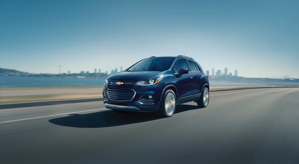 A dark blue 2021 Chevy Trax is driving away from a city in front of a river.