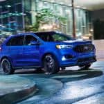 A blue 2021 Ford Edge ST is rounding a corner at night with its lights illuminated.