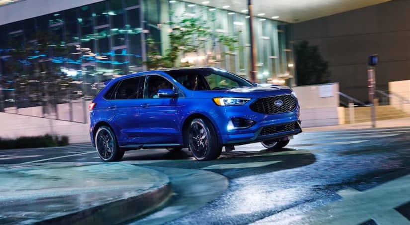A blue 2021 Ford Edge ST is rounding a corner at night with its lights illuminated.