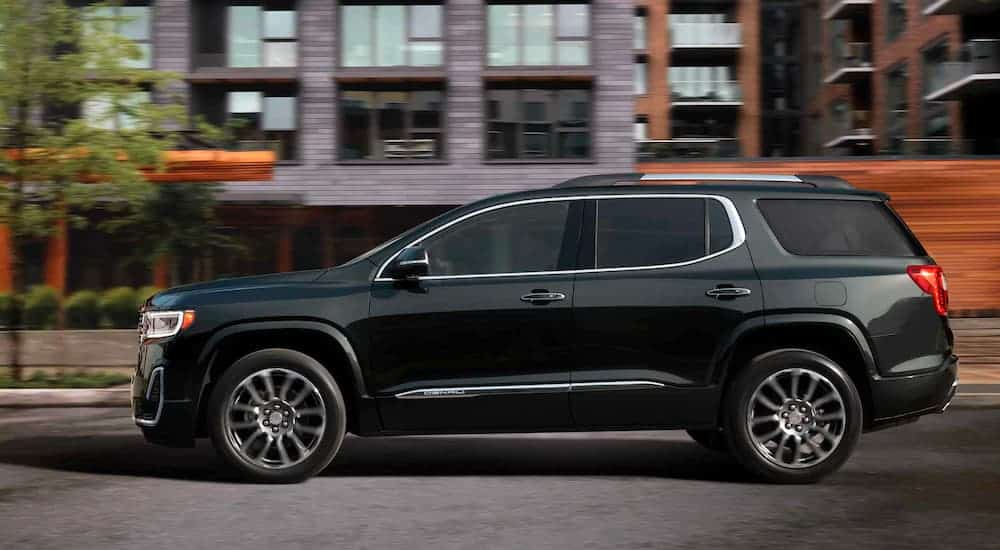 A black 2021 GMC Acadia Denali is shown from the side driving past blurred building.