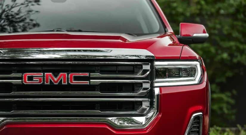 A close up shows the front grill and headlight on a red 2021 GMC Acadia.