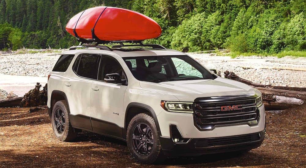A white 2021 GMC Acadia AT4 is shown parked next to a river with a kayak on the roof.