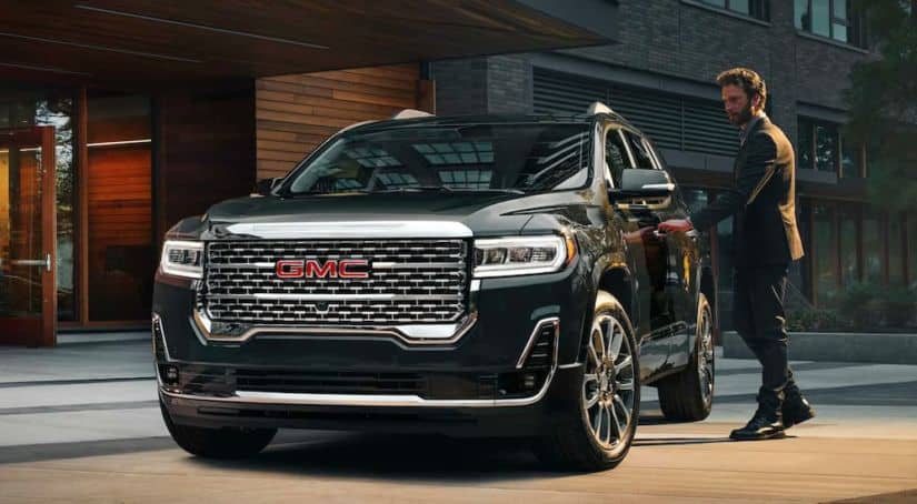 A man in a suit is shown opening the door of a black 2021 GMC Acadia Denali.