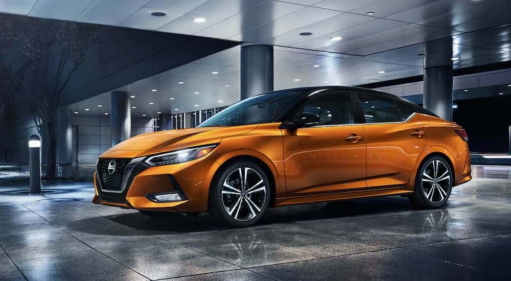 An orange 2021 Nissan Sentra is parked under an overhang at a modern building at night.