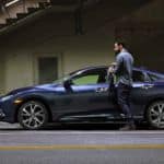 A man is getting into a blue 2021 Honda Civic under a bridge after winning the 2021 Honda Civic vs 2021 Toyota Corolla comparison.
