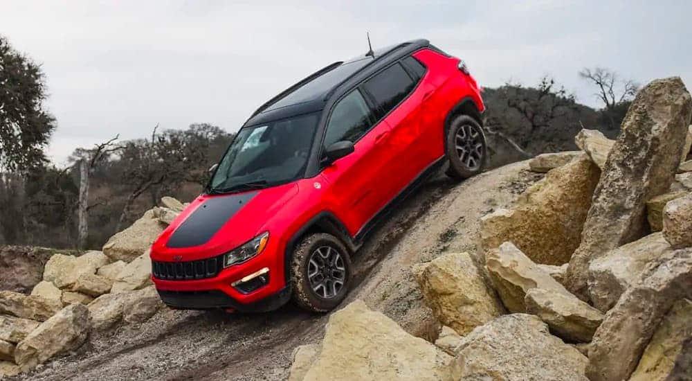 A red 2021 Jeep Compass Trailhawk is driving over rocks.