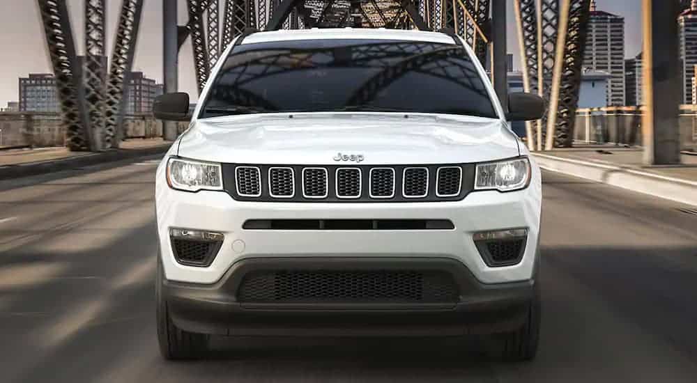 A white 2021 Jeep Compass is shown from the front driving over a steel bridge.