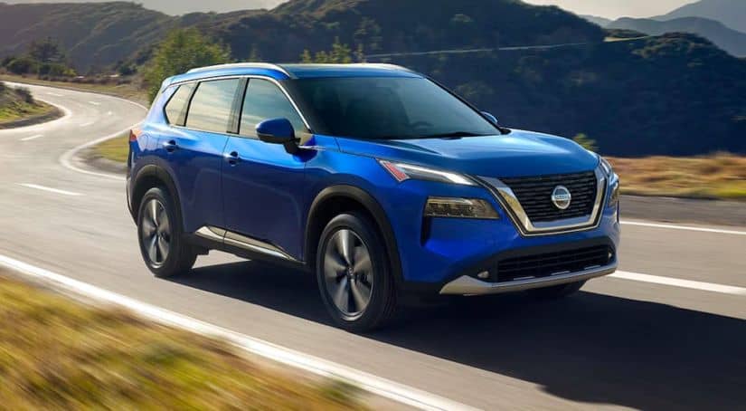 A blue 2021 Nissan Rogue is shown from the side driving down a winding road.