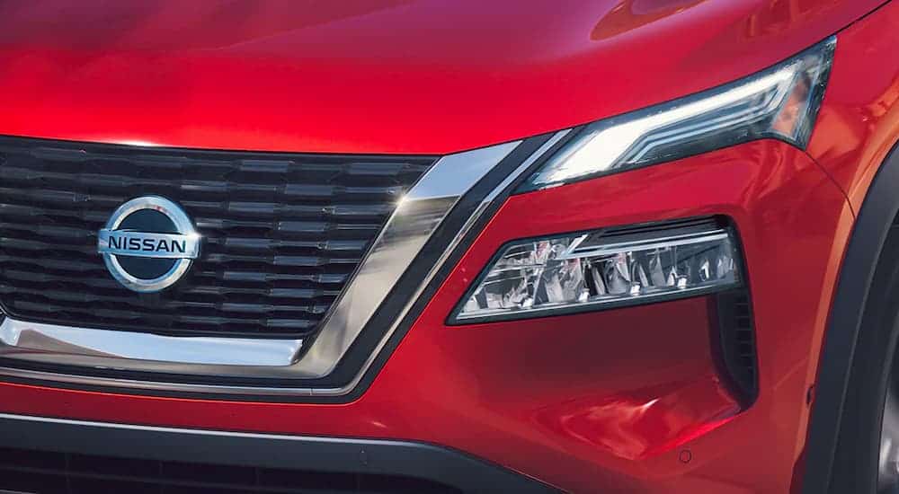 A close up shows the grill and headlight on a red 2021 Nissan Rogue.