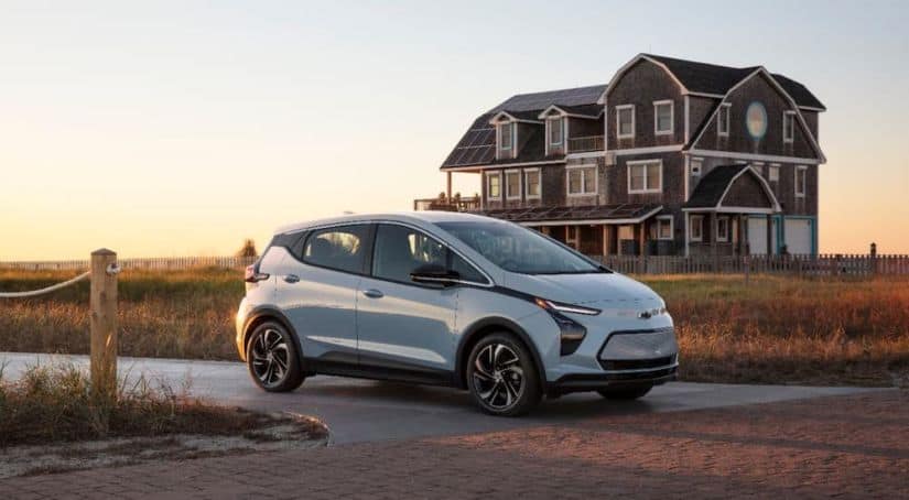 A pale blue 2022 Chevy Bolt EUV is parked in front of a beach house at sunset.