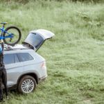A woman is shown taking a bike off of the roof rack of a gray SUV.