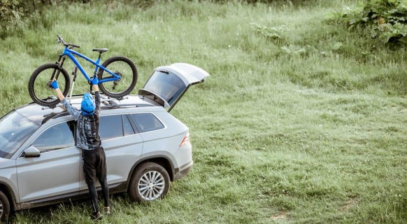 A woman is shown taking a bike off of the roof rack of a gray SUV.
