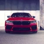A red 2021 BMW M5 is shown from the front while parked in front of a concrete wall after getting a great BMW lease deal.