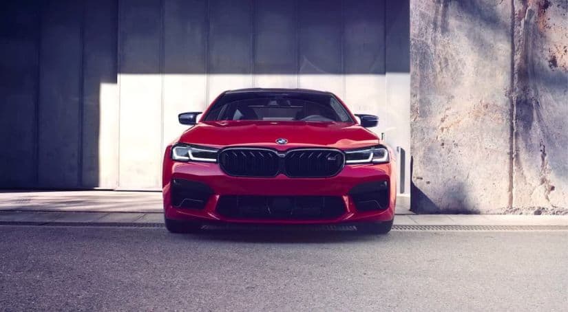 A red 2021 BMW M5 is shown from the front while parked in front of a concrete wall after getting a great BMW lease deal.