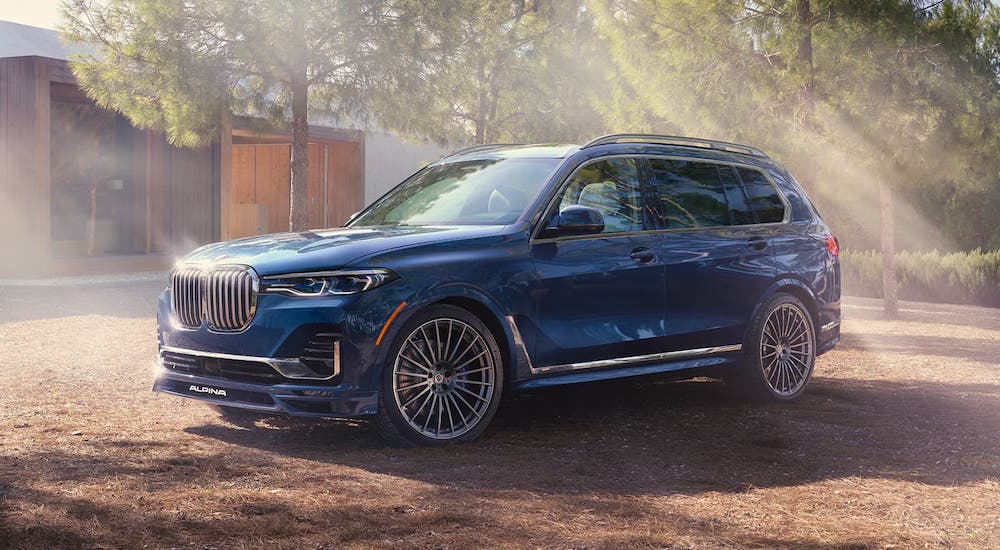 A blue 2021 BMW X7 is parked in front of a modern cabin in the woods.