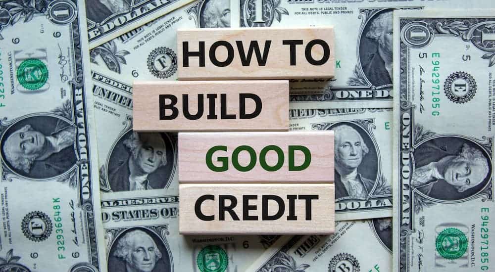 Wooden blocks are on top of money saying 'how to build good credit' at a buy here, pay here dealership.
