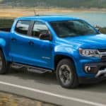 A blue 2021 Chevy Colorado from a Chevy dealer is driving past a lake.