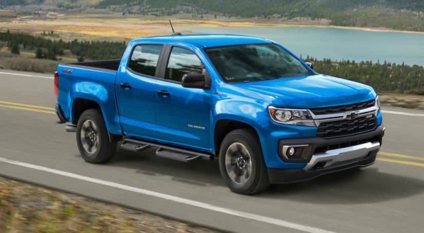 A blue 2021 Chevy Colorado from a Chevy dealer is driving past a lake.