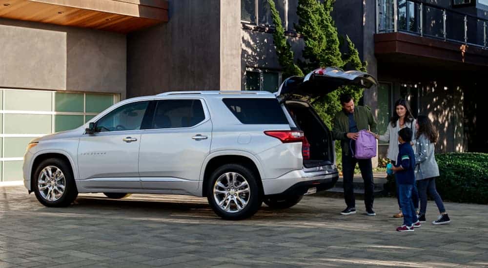 A family is near the open trunk of a silver 2021 Chevy Traverse in front of a garage.