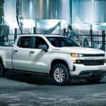 A white 2021 Chevy Silverado 1500 is having cooper barrels loaded into the bed by a forklift.