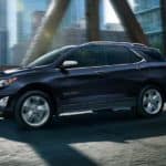 A blue 2021 Chevy Equinox, a popular Chevy SUV, is driving on a city bridge.