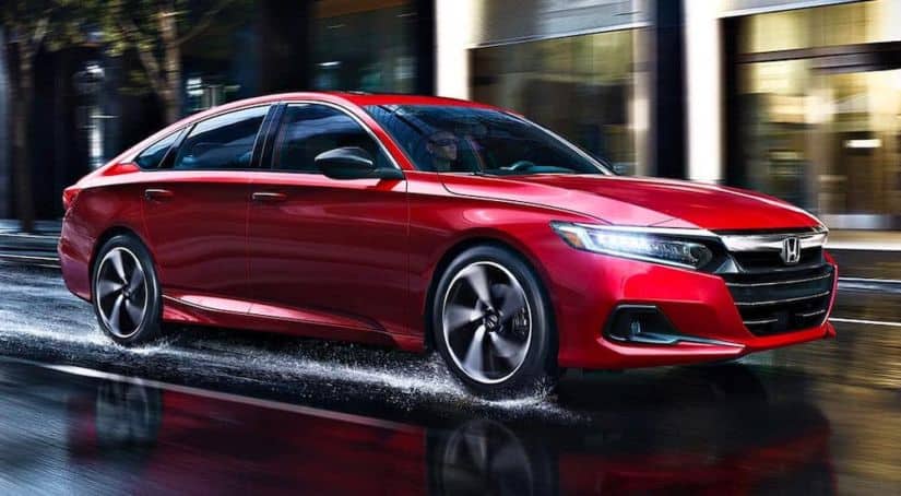 A red 2021 Honda Accord is driving on a wet city street.