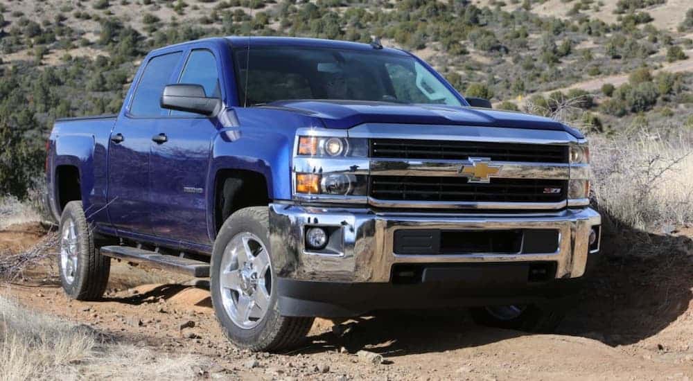 A blue 2015 Chevy Silverado 2500HD is driving on a dirt road in a desert.