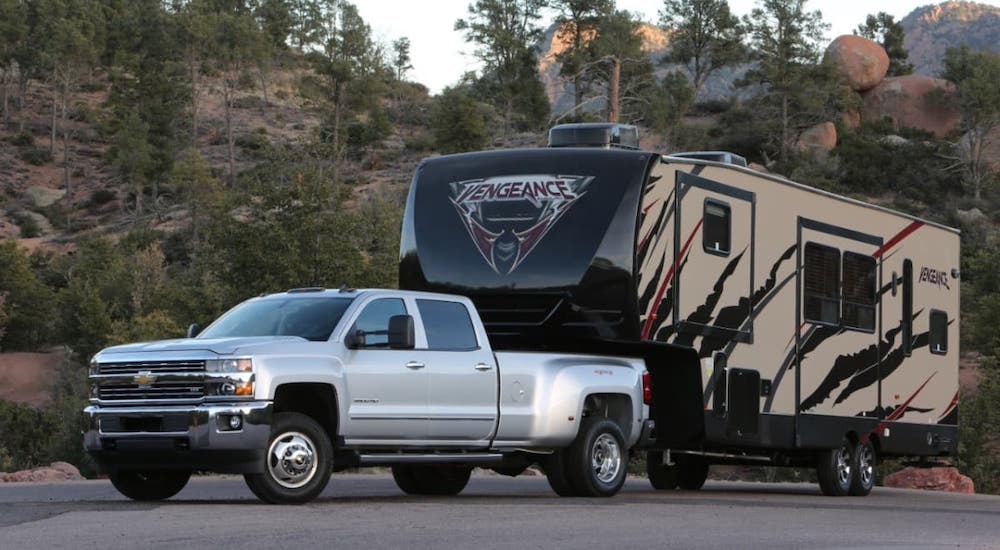 A silver 2018 pre-owned Chevy 3500HD is parked while towing a large camper.