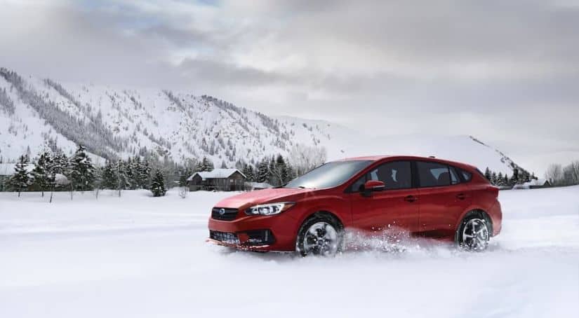 A red 2020 Subaru Impreza is shown driving in the snow after leaving a Subaru dealer near you.