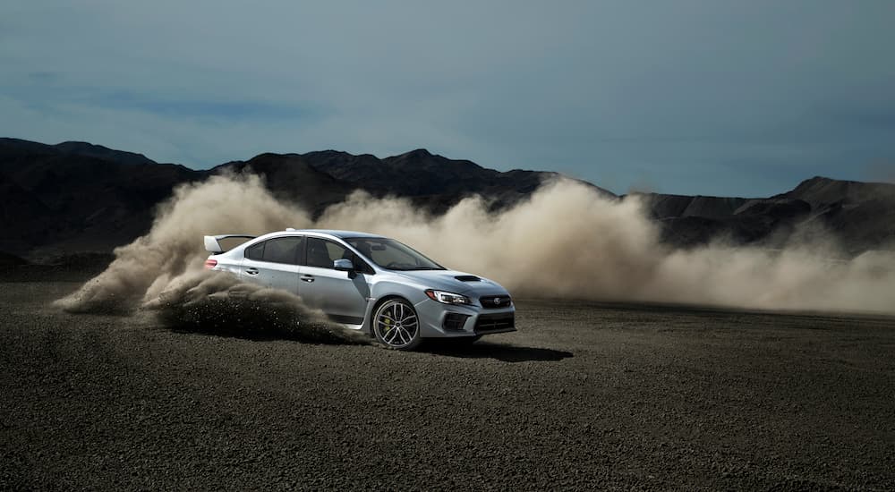 A silver 2020 Subaru WRX STI is shown doing doughnuts on an empty dirt lot.