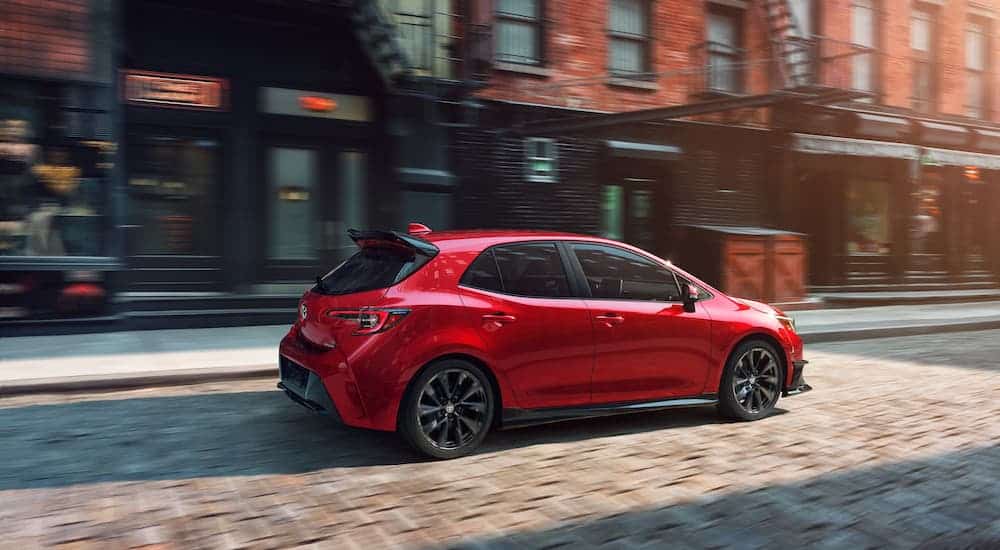 A red 2021 Toyota Corolla Hatchback is driving on a city street.