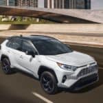 A popular Toyota lease deal, a white 2021 Toyota RAV4, is shown from a high angle driving past a bridge.
