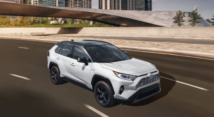 A popular Toyota lease deal, a white 2021 Toyota RAV4, is shown from a high angle driving past a bridge.