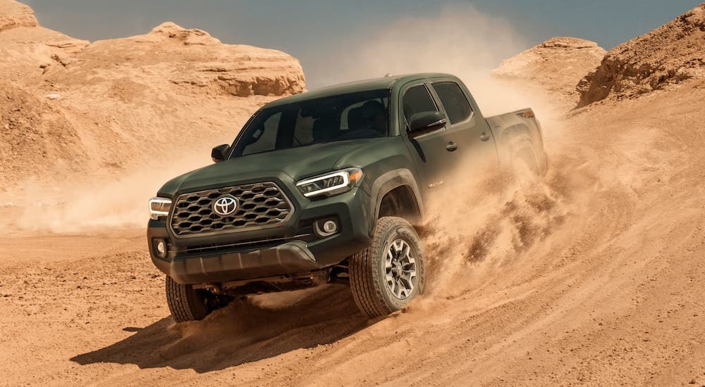 A green 2021 Toyota Tacoma is driving in sand.