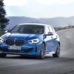 A popular used BMW near me, a blue 2019 BMW M135i, is driving down a winding road.