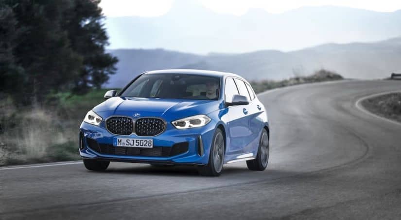 A popular used BMW near me, a blue 2019 BMW M135i, is driving down a winding road.