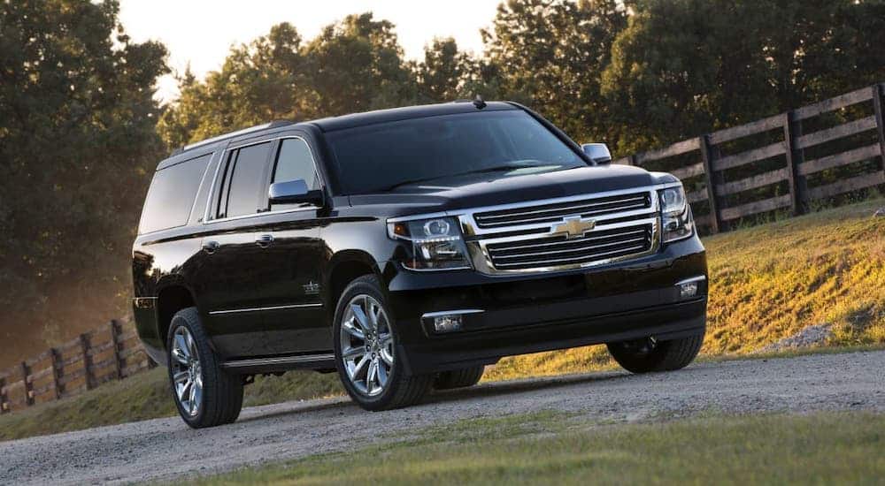 A black 2015 Chevy Suburban is driving in front of a wooden fence.
