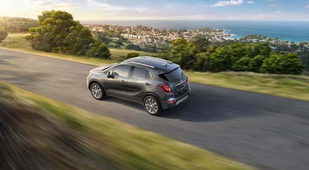 A gray 2017 Buick Encore is driving on a highway overlooking a town and shown from a high angle.