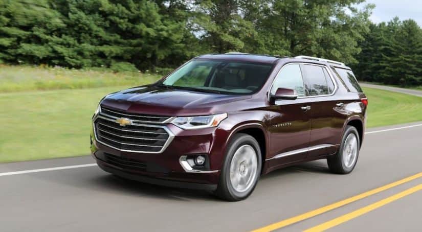 A burgundy 2018 Chevy Traverse is driving around a winding road in front of trees after leaving a used car dealer.