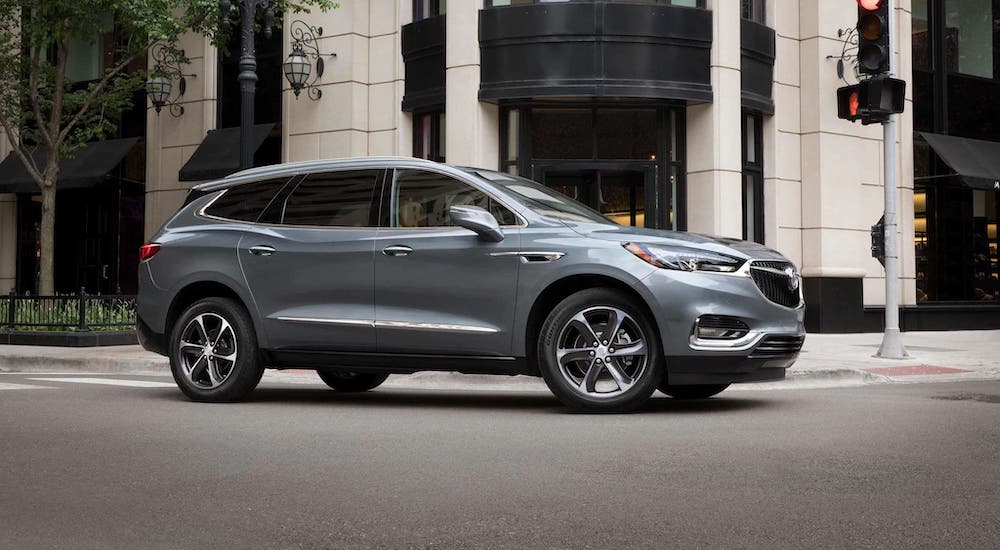 A gray 2019 Buick Enclave is driving on a city street after leaving a used car dealer.