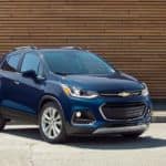 A blue 2019 Chevy Trax from a used Chevy dealership is parked in front of a wooden wall.