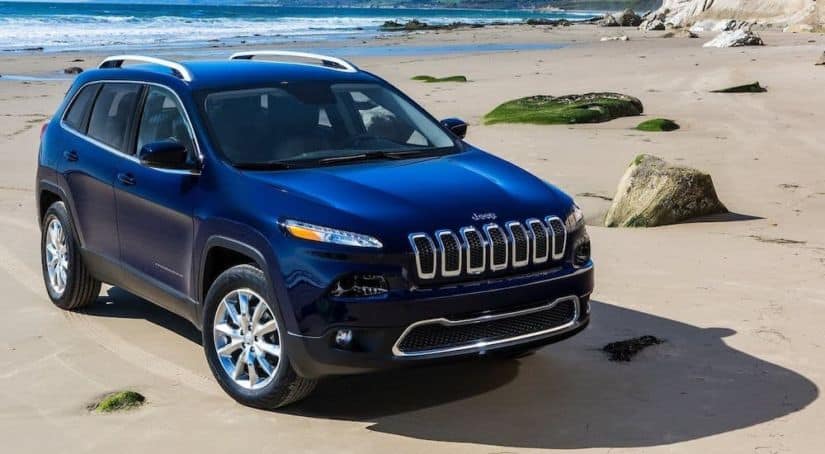 A blue 2013 Jeep Cherokee is parked on a beach.