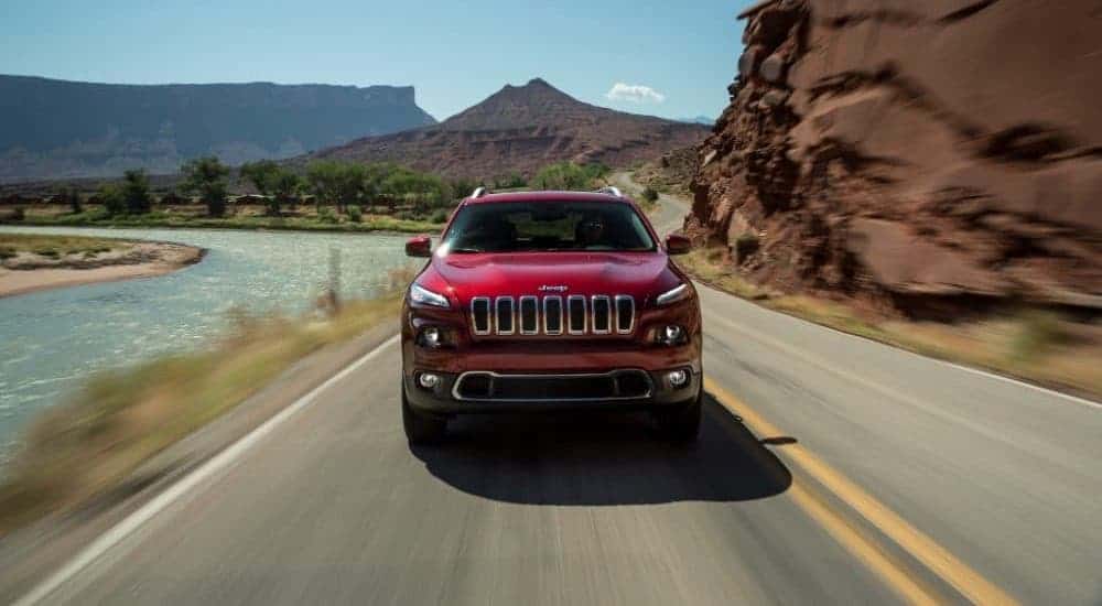A red 2017 Jeep Cherokee is shown from the front driving on a highway next to a river.