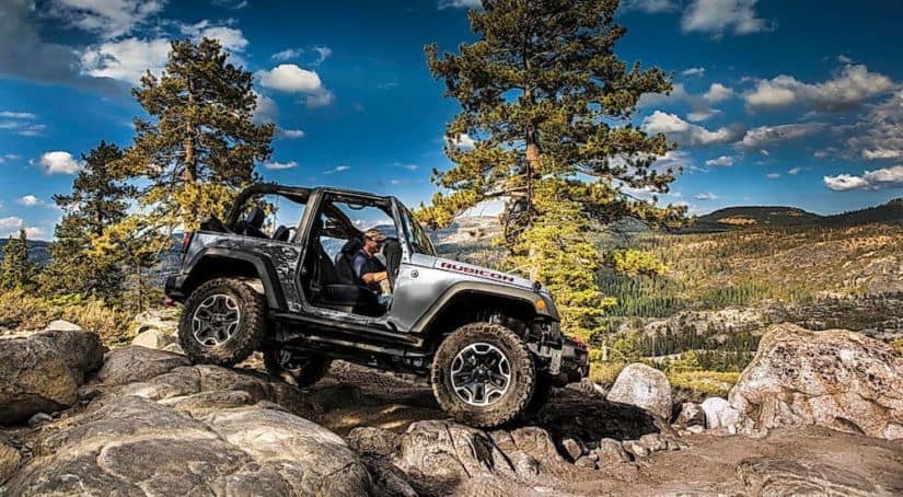 A silver 2017 Jeep Wrangler with no roof or doors is crawling over rocks.