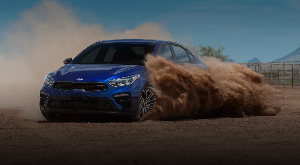 A blue 2020 Kia Forte is kicking up dirt in a field.