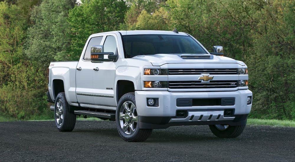 A white 2017 Chevy Silverado 2500HD from a used truck dealer is parked in front of trees.