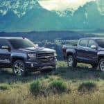 A grey 2018 Chevy Silverado and grey 2018 Colorado are in a field in front of mountains.