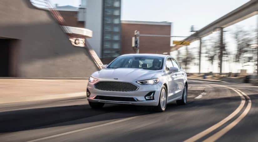 A white 2020 Ford Fusion is driving on a city street as part of the 2020 Ford Fusion vs 2021 Honda Accord comparison.