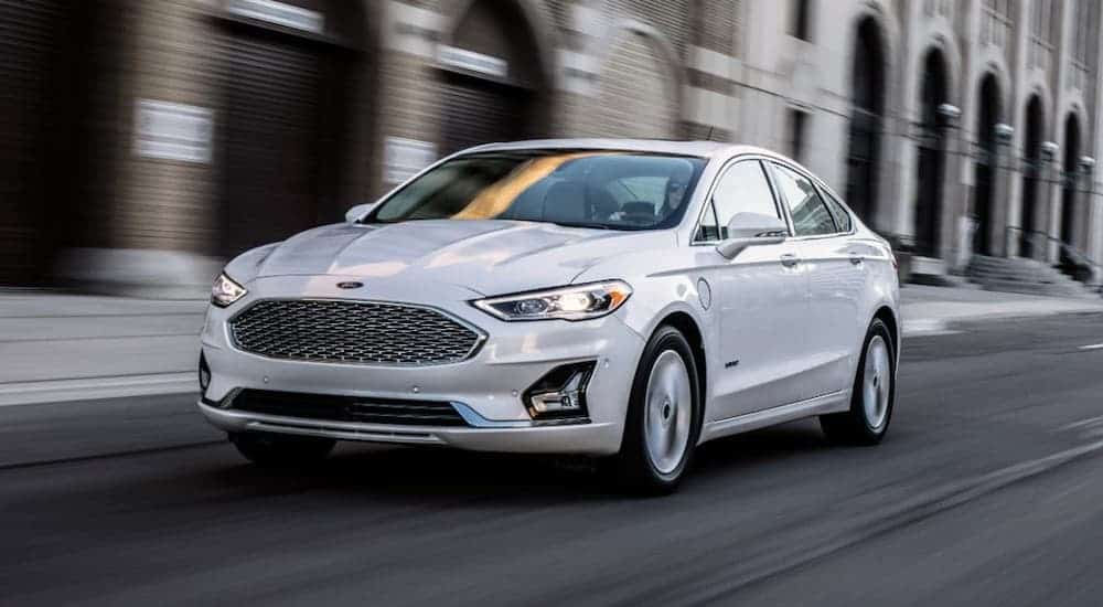 A white 2020 Ford Fusion Hybrid is driving on a city street.