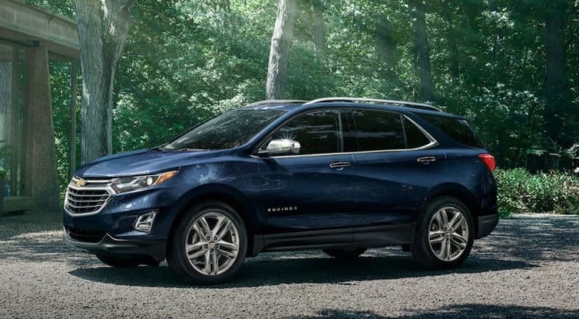 A blue 2021 Chevy Equinox is parked in front of trees after winning the 2021 Chevy Equinox vs 2021 Toyota RAV4 comparison.